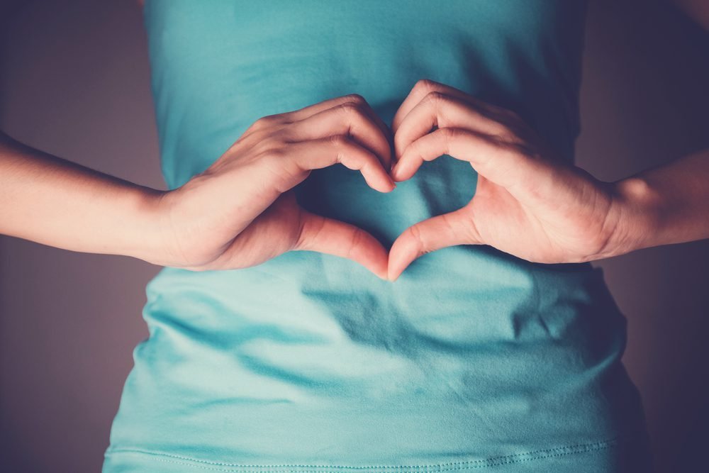 Woman hands making a heart shape on her stomach.